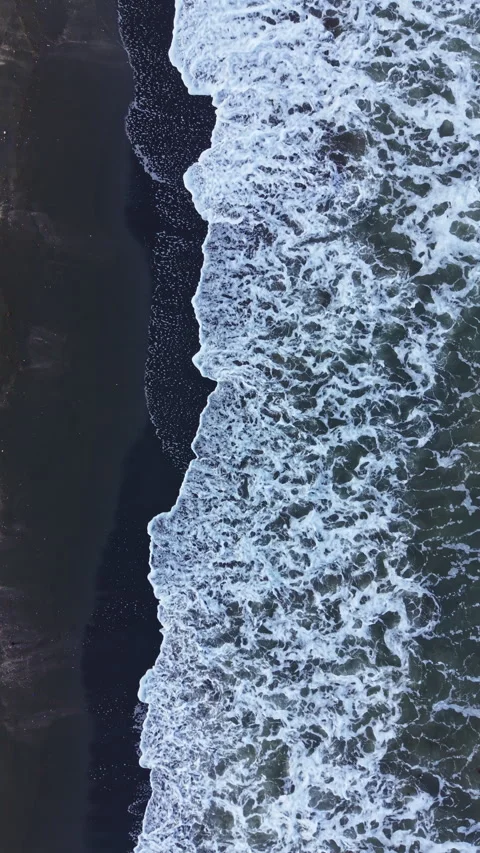 Waves crash on dark sand at the beach during the day with foam forming along the 库存影片 337907118