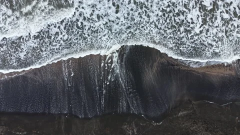 Waves crash on a dark sandy beach during daytime, showing the powerful motion of Stock Footage 335389208