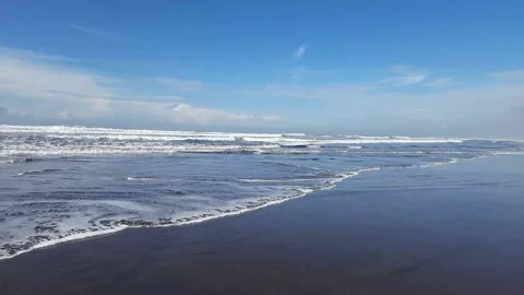 Waves crash onto the dark wet sand under a bright blue sky Video stock 328640489