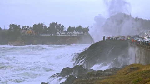 Waves crash dramatically against the rocks and seawall as storm watchers gather 库存影片 329145217