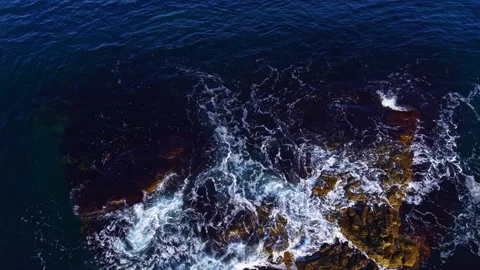 Waves crash dramatically over rugged rocks as the sun sets gently over the Stock Footage 332065587
