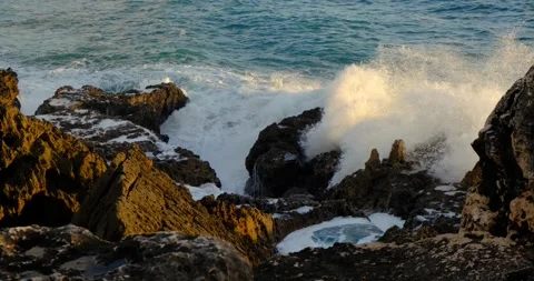 Waves crash force against jagged coastal rocks of Cascais, Portugal Stock Footage 309654739