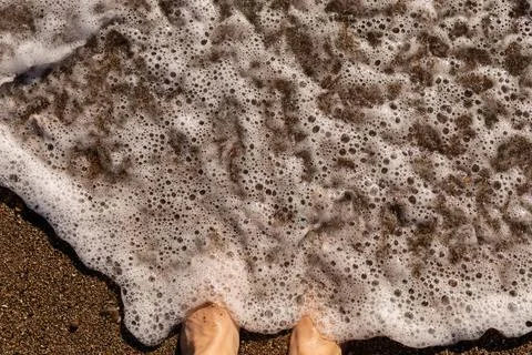 Waves crash gently on the shore, creating foam around bare feet. The sand is  Stock Photos