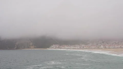Waves crash on the main beach in Nazare, Portugal. The city and the rocks in the Stock Footage 257332050