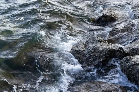 Waves crash over barnacle-covered rocks Stock Photos