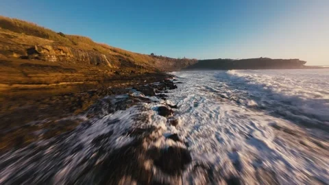 Waves crash over dark, wet rocks at golden hour Stock Footage 339788330