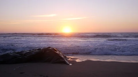 Waves crash over rock on beach as sun sets on horizon Stock Footage 104684205
