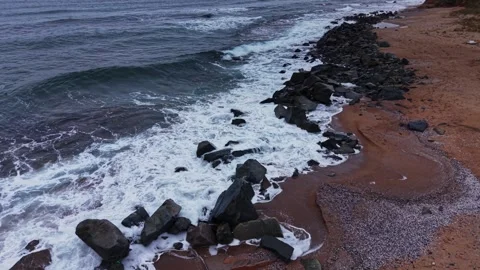 Waves crash on rocks along a sandy beach near the ocean's edge Vidéo 331296337
