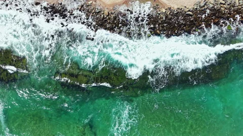 Waves crash on rocks along the shore in a coastal area during daytime with clear 스톡 동영상 344824023