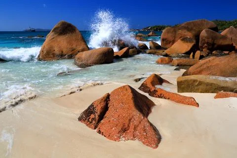 Waves crash on rocks at a beautiful beach with clear water and bright sunlight Stock Photos