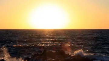 Waves crash on rocks as the sun rises high over the horizon Stock Footage 85894028