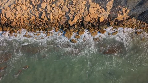 Waves crash on rocky shore during sunset at a beach Stock Footage 346017732