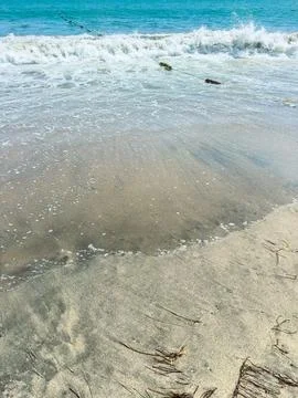 Waves crash on sandy beach with a clear blue sea under warm sunlight Stock Photos