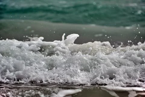 Waves crash on sandy beach creating splashes and foam during sunny day Stock Photos