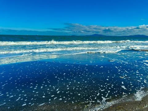 Waves crash on a sandy beach during a sunny day with blue sky and clouds ov.. Stock Photos