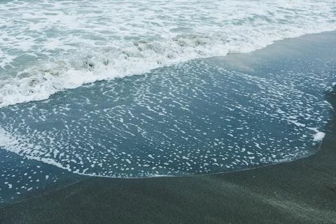 Waves crash onto a sandy beach as evening approaches. Foam forms where the wa Stockfoto's