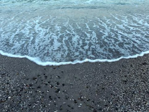 Waves crash on a sandy beach with small pebbles and shells under a clear sky Фото