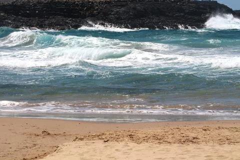 Waves crash on a sandy beach under a clear sky during midday at a coastal l.. Stock Photos