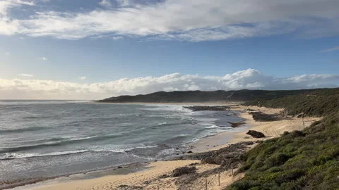 Waves crash on a sandy beach while clouds pass over the coastline Stock Footage 337497564