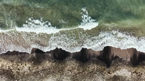 Waves crash on a sandy beach while foam forms along the shore in a coastal area 库存影片 337878025