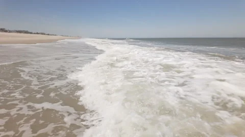 Waves crash onto sandy coastline shore under clear sky Stockbeeldmateriaal 337181554