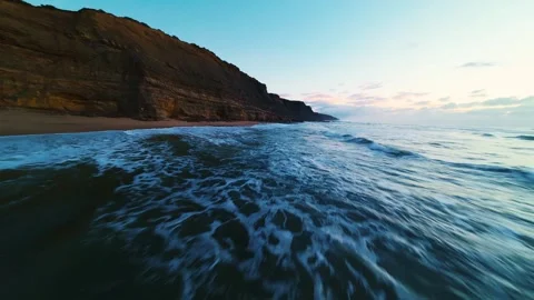 Waves crash onto sandy shore against rocky cliff face Stock Footage 340914863