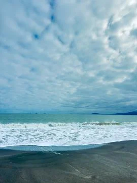 Waves crash on a sandy shore beneath a cloudy sky near the ocean during the.. Stock Photos