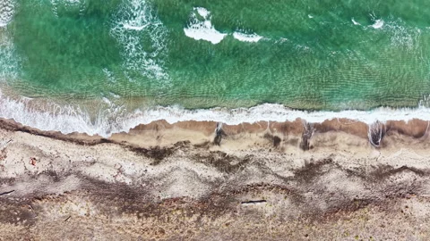Waves crash on sandy shore during daytime with clear ocean water and patterns in Vidéo 344779291