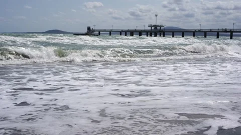Waves crash onto the sandy shore under a partly cloudy sky Stock Footage 315443346