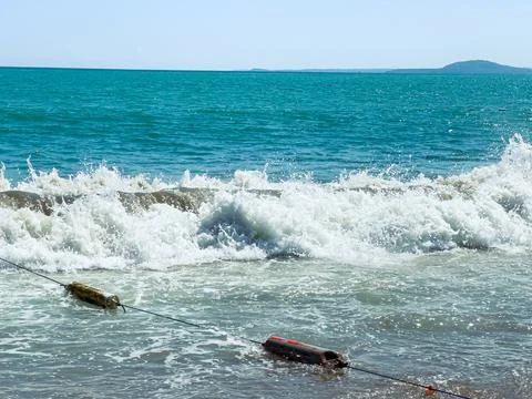 Waves crash onto the sandy shore while a line of floats is anchored in the wa Stock Photos