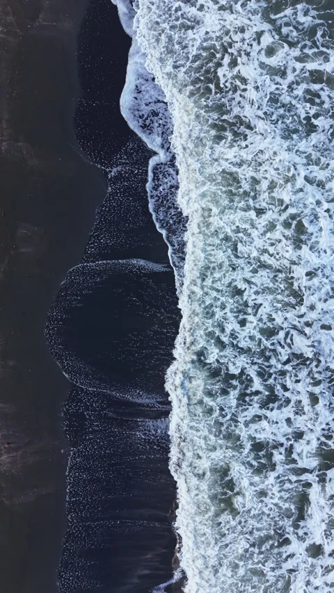 Waves crash on the shore at a beach during midday, creating a pattern with foam Stock Footage 337907116