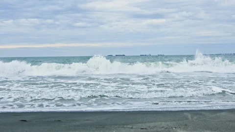 Waves crash on the shore at a beach with ships in the distance during an Stock Footage 340176101