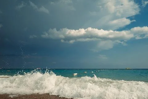 Waves crash on shore, creating foam as dark clouds fill the sky above. Boats Stock Photos