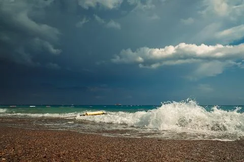 Waves crash on shore, creating foam as dark clouds fill the sky above. Boats Stock Photos