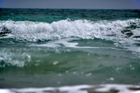 Waves crash on the shore during a cloudy day at the beach, showcasing ocean.. Stock Photos