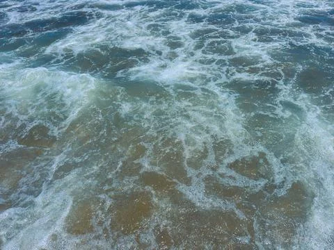 Waves crash on the shore during the day at a beach with clear water and foa.. Stock Photos