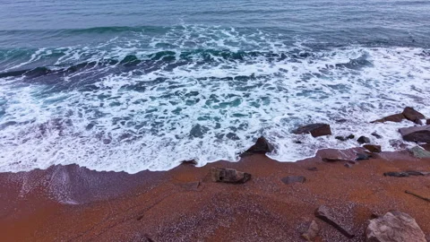 Waves crash on shore with rocks scattered on sandy beach in late afternoon sun Stock Footage 331954083