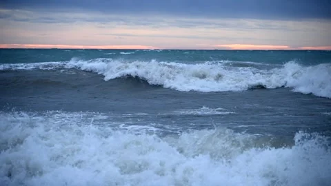 Waves Crash on the Shore as the Sun Sets Over a Stormy Sea in This Dramatic Slow Stock Footage 327616488