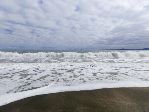 Waves crash on the shore under a cloudy sky near a beach during the day Stock Photos
