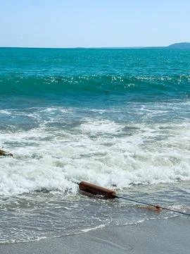 Waves crash on the shore while a buoy floats near the beach under a clear sky Stock Photos