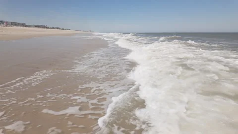 Waves crash in slow motion onto sandy shore under clear blue sky Stockbeeldmateriaal 337180745