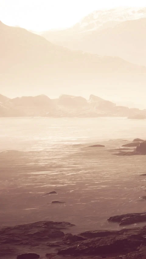Waves crash softly against rocks on a foggy beach during the early morning Stock Footage 338377797