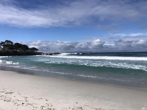 Waves Crash on a Tranquil Beach Under a Vast Blue Sky Stock Photos
