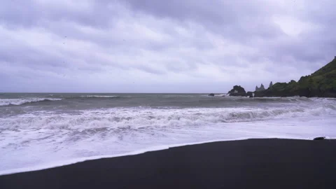Waves crash on Vik's black sand beach under an overcast sky 스톡 동영상 327082704