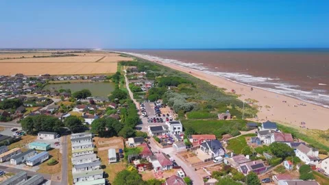 Waves crash onto wide sandy beach under clear blue sky. Fields stretch beyond Stock Footage 341473747