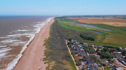 Waves crash onto wide sandy beach under clear blue sky. Fields stretch beyond Stock Footage 342025200