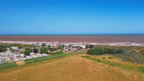 Waves crash onto wide sandy beach under clear blue sky. Fields stretch beyond Stock Footage 342025276