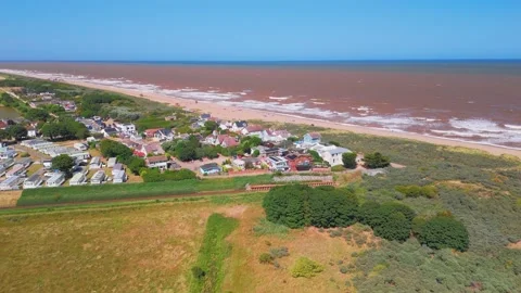 Waves crash onto wide sandy beach under clear blue sky. Fields stretch beyond Stock Footage 342025321