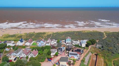 Waves crash onto wide sandy beach under clear blue sky. Fields stretch beyond Stock Footage 342025378