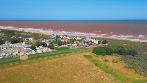 Waves crash onto wide sandy beach under clear blue sky. Fields stretch beyond Stock Footage 342025410
